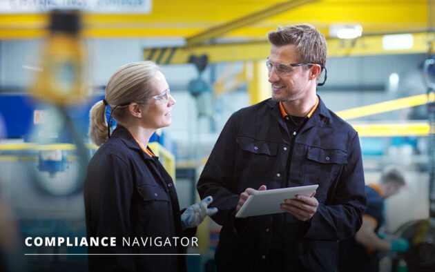 Two people in a warehouse talking while holding a tablet. Both are wearing protective eyewear