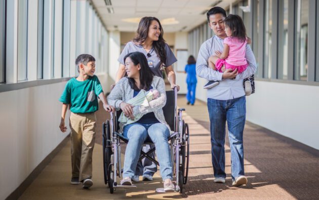 Family walking in a hospital. A nurse pushes the mother holding a newborn in a wheelchair