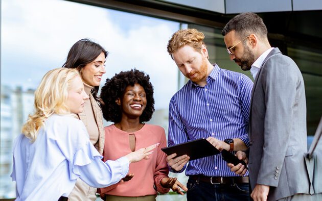 Group of people in business attire huddled around a man holding a tablet